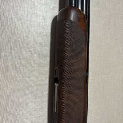 Arma longa com coronha em madeira castanha texturada e parte metálica preta.