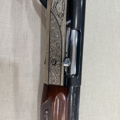 Espingarda de calibre 12 com madeira castanha e parte metálica azulada gravada