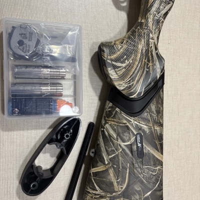 Coronha de espingarda camuflada com acessórios de limpeza e tubos metálicos ao lado