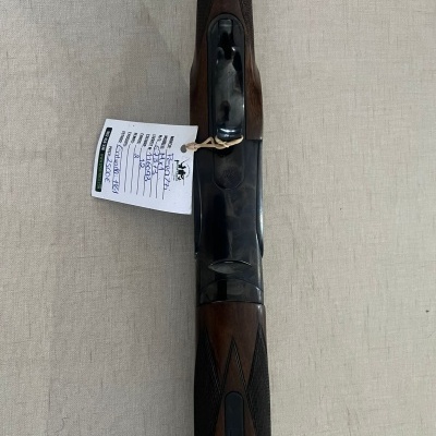 espingarda com estrutura metálica preta e coronha em madeira com padrão entalhado e etiqueta branca