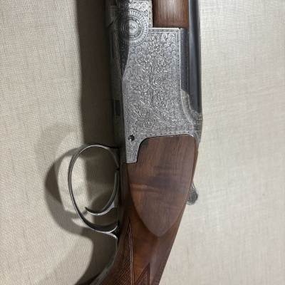 Parte de arma com coronha em madeira escura e detalhes metálicos gravados