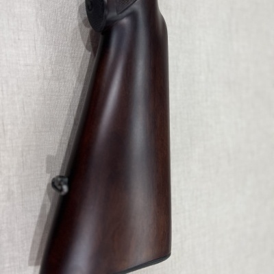 Coronha de espingarda em madeira escura com textura antiderrapante encostada na parede