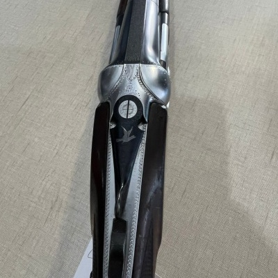 Espingarda de canos paralelos com madeira escura e detalhes metálicos prateados