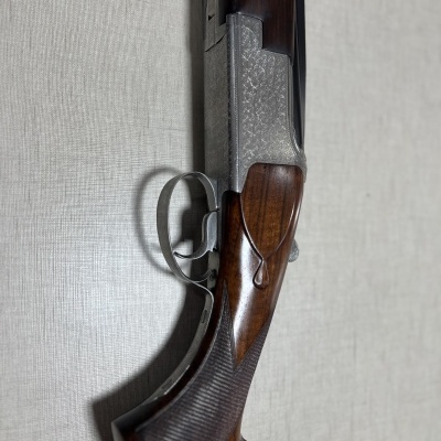 Espingarda com punho de madeira e acabamento metálico contra uma parede bege