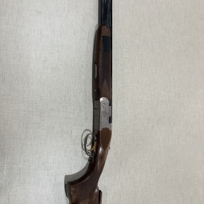 Espingarda de caça com madeira castanha e metal prateado sobre fundo cinzento