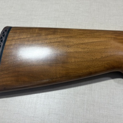 Coronha de madeira castanha com acabamento polido e borracha preta na extremidade sobre fundo cinza claro.