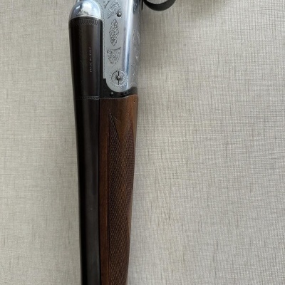 Espingarda em madeira e metal com gravações decorativas sobre fundo claro.