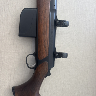 Espingarda SAUER 303 com coronha de madeira e corpo metálico preto em fundo claro.