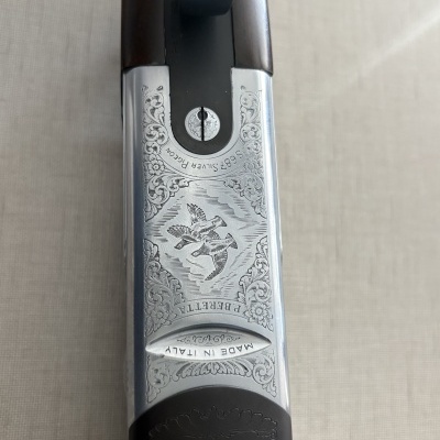 Parte superior de uma espingarda Beretta com metal prateado gravado e madeira castanho escuro