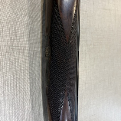 Cabo em madeira trabalhada e metal prateado de arma de fogo encostada numa parede clara