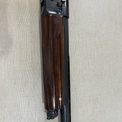 Parte da espingarda com coronha de madeira escura e cano preto sobre fundo claro