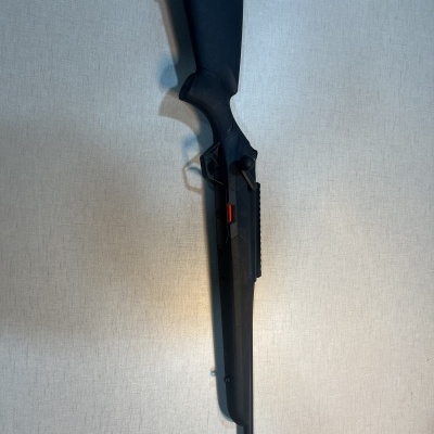 Espingarda preta com detalhe vermelho encostada numa parede clara