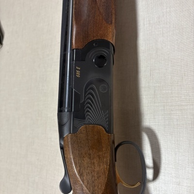 Espingarda de caça com madeira castanha e corpo metálico preto gravado.