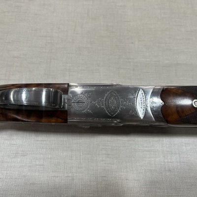 Espingarda de cano duplo com corpo prateado e punho em madeira escura com gravações e texto