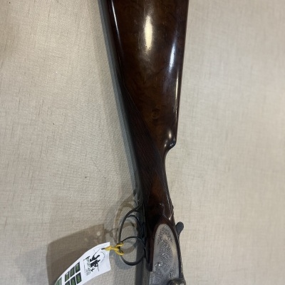 Espingarda de madeira castanha escura e metal prateado com etiqueta branca num fundo neutro