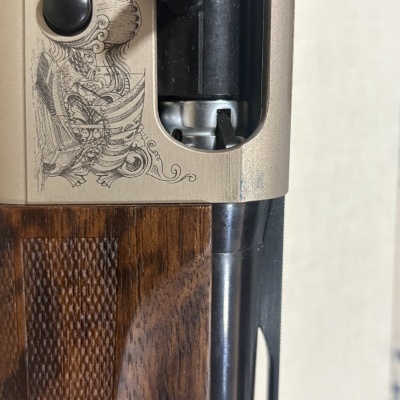 Detalhe de espingarda com coronha em madeira castanha e parte superior metálica bege com gravações e texto