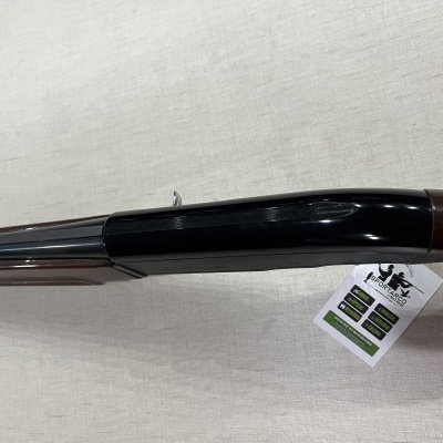 Espingarda com cano prateado e coronha em madeira com etiqueta, sobre tecido claro