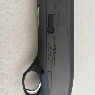 Parte lateral de uma arma de caça preta com empunhadura em madeira castanha e texto impresso