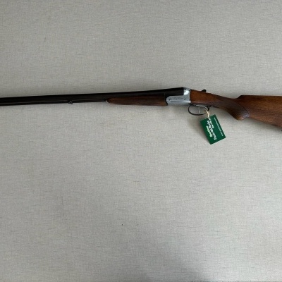 Espingarda de madeira e metal com etiqueta verde sobre superfície clara