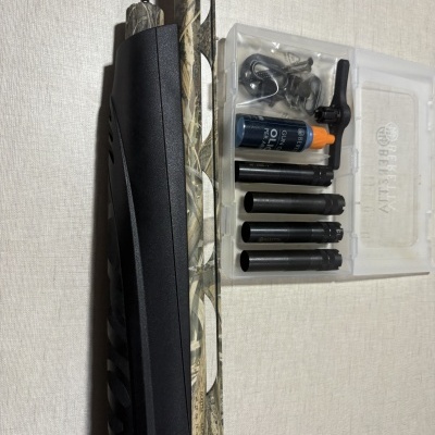 Espingarda camuflada com acessórios e óleo lubrificante BERETTA numa caixa transparente