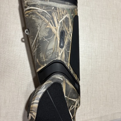 Parte traseira de arma camuflada com padrão de vegetação e detalhes em preto
