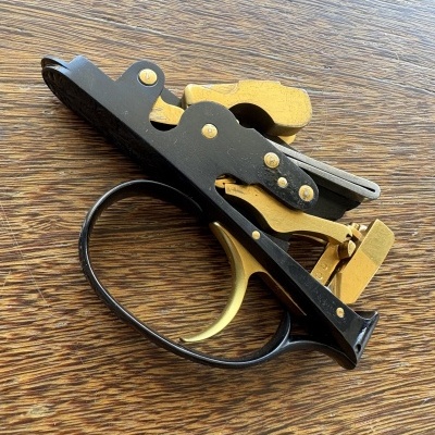 Mecanismo de gatilho de arma em metal preto e dourado sobre mesa de madeira