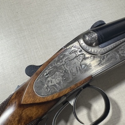Espingarda de canos duplos com gravações em metal e empunhadura em madeira castanha.