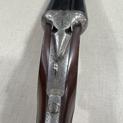 Espingarda de canos paralelos com madeira escura e detalhes metálicos gravados