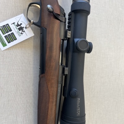 Carabina com coronha de madeira e luneta preta com inscrições nas lentes, com etiqueta pendurada