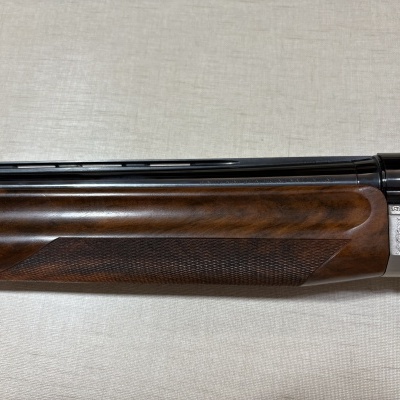 Parte de arma de fogo em madeira castanha e metal prateado com gravações e texto Benelli Armi