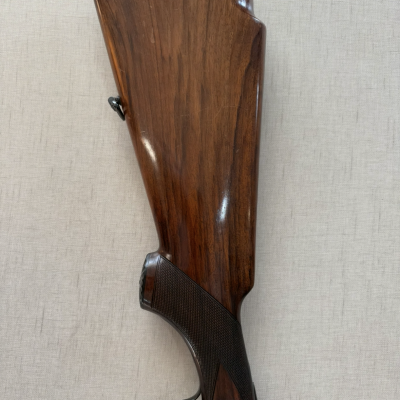 Espingarda de madeira polida com detalhes metálicos decorativos sobre fundo claro