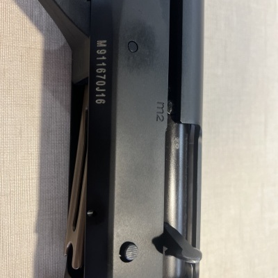 Parte lateral de arma de fogo preta com números e gravações visíveis