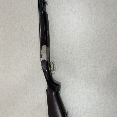 Espingarda de canos paralelos com partes em madeira escura e metal preto em fundo claro