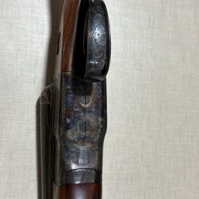 Espingarda em madeira escura com metal gravado e fundo bege texturizado