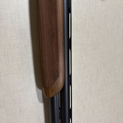 Coronha de madeira e cano metálico de espingarda com fundo claro.