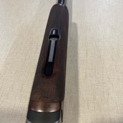 Espingarda com cabo de madeira escura e cano metálico prateado sobre superfície clara