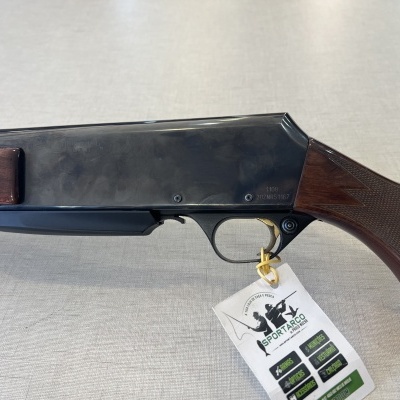 Espingarda com corpo metálico preto e partes em madeira castanha com textura, com etiqueta branca pendurada