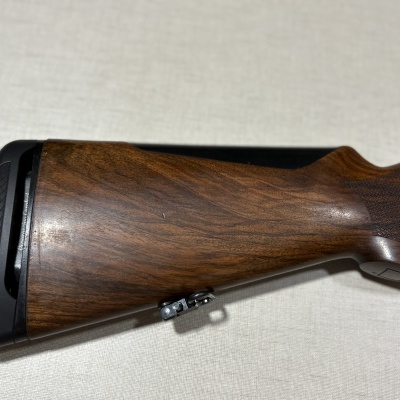 Coronha de rifle em madeira castanha polida com peça emborrachada preta na extremidade.
