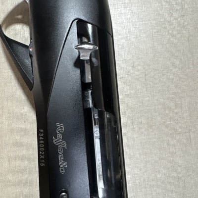 Arma de fogo preta da marca Raffaello com texto visível sobre superfície bege.