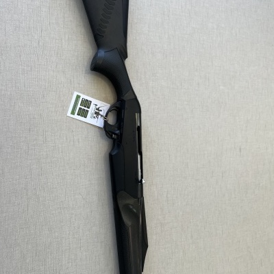 Espingarda preta com etiqueta branca sobre superfície cinzenta.