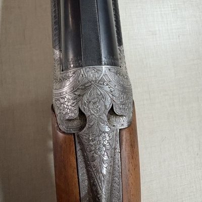 Espingarda dupla em madeira com gravações florais no metal.