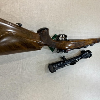 Rifle em madeira castanha com bipé preto sobre superfície clara