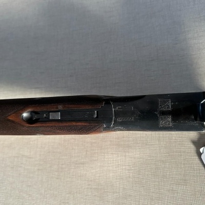 Espingarda de madeira escura e metal negro com etiqueta branca numa superfície clara