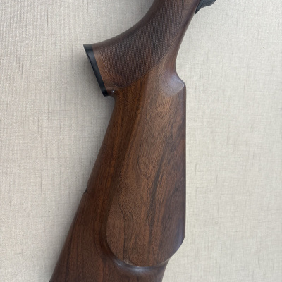 Punho de madeira castanha de uma espingarda com textura quadriculada e base preta.