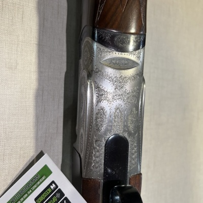 Espingarda em madeira castanha e metal prateado com gravações, junto a panfleto com texto em português.