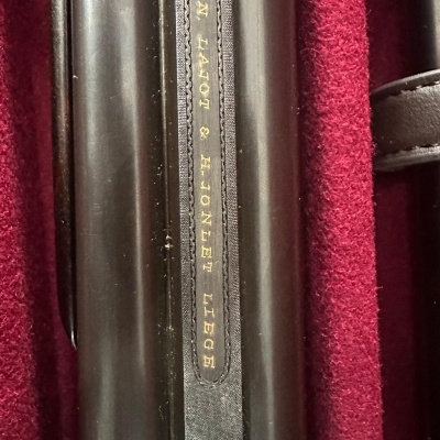 Cinta de couro preta com texto dourado sobre objeto preto dentro de caixa vermelha