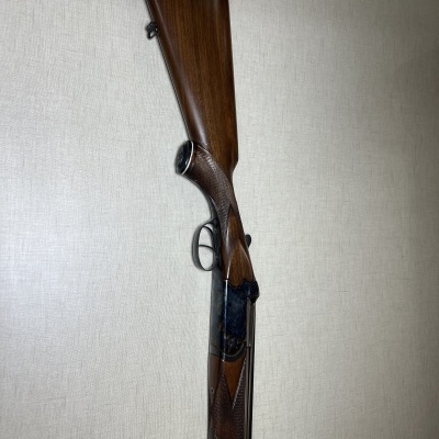 Espingarda de canos duplos com coronha em madeira com detalhes entalhados e metal preto, numa parede clara