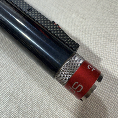 Detalhe de objeto cilíndrico preto com anel vermelho e acabamento metálico prateado.