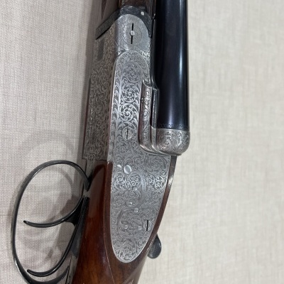 Espingarda de canos duplos com gravação detalhada em metal e madeira castanha escura.