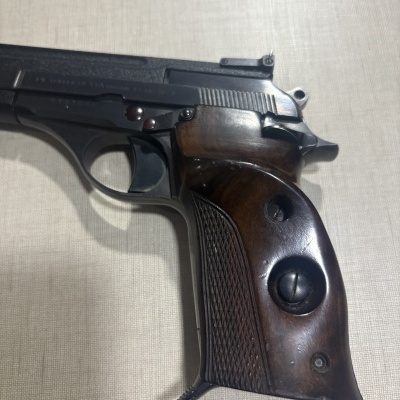 Pistola com empunhadura em madeira escura e estrutura metálica preta